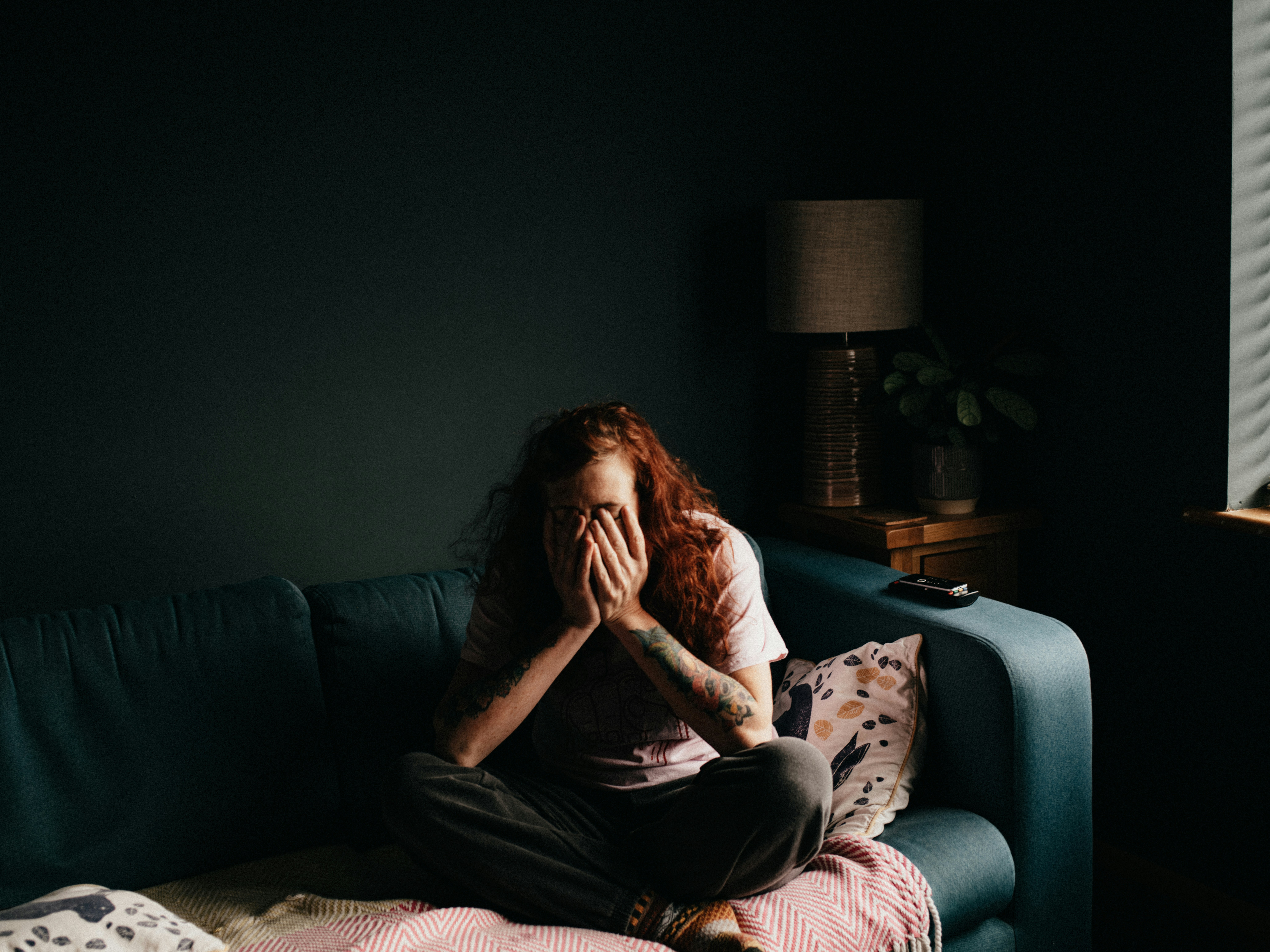A person sitting quietly with their hands over their face, representing emotional stress and mental health challenges.